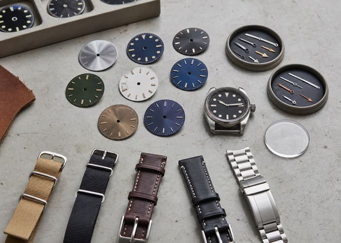 A collection of custom watch dials, straps, and hands, all components of the total quartz watch manufacturing cost.